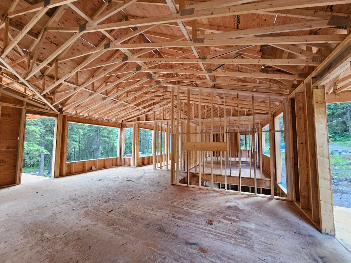 Interior of a framed great room under roof trusses with large window openings