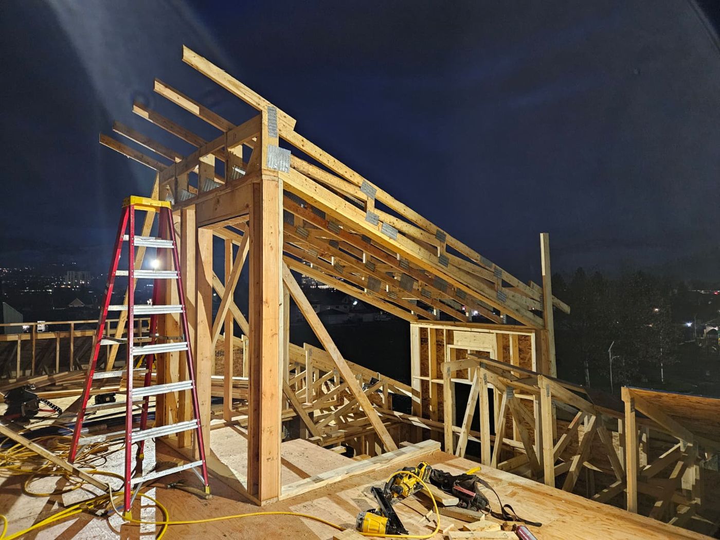 Roof framing at night with a red ladder and nail gun